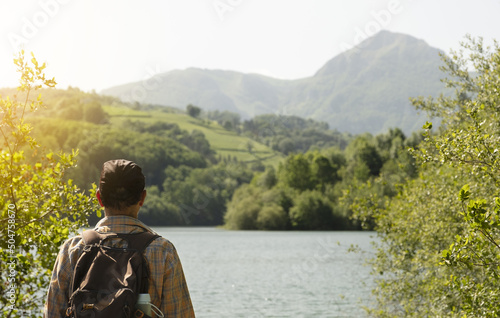 Traveler with backpack looking at the lake and the mountain