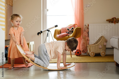 Children playing on balance Board for Toddlers in kids room. Curvy Rocker Board used for motor physical development at home. Girl and boy playing, get fit, stretch back in yoga exercises  photo