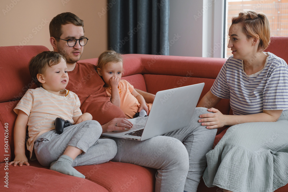 Big happy family watching movies playing games on laptop. Mother father kids spending time with gadgets on sofa Children with parents looking on computer screen at home Siblings playing with console Big happy family watching movies playing games on laptop. Mother father kids spending time with gadgets on sofa Children with parents looking on computer screen at home Siblings playing with console