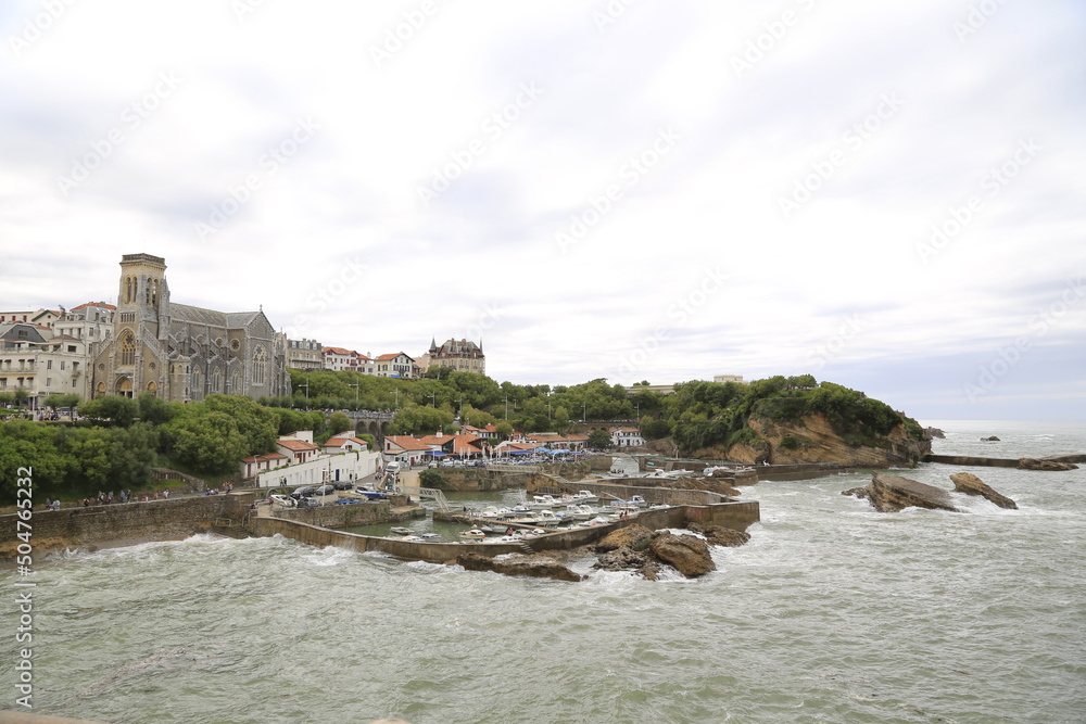 Beach landscape France: Boardwalk of Biarritz with the old fishing harbor and church Eglise Saint-Martin of Biarritz at stormy weather with breakers at the bay of Biscay in the Atlantic Ocean