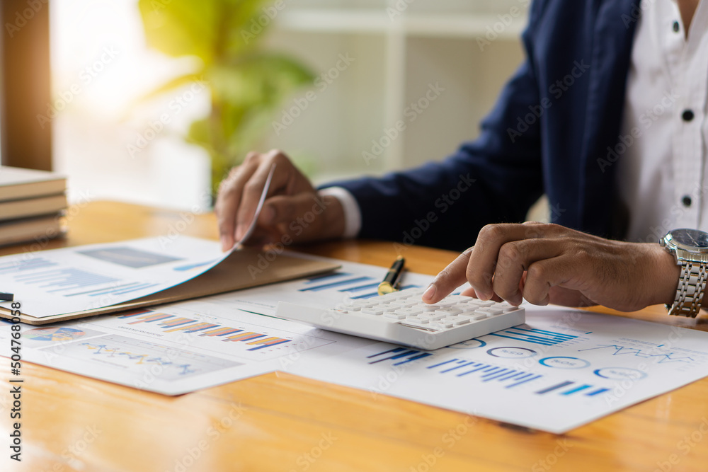 Businessman hand pressing a calculator calculation concept The front view of the hand points to the data from the business data chart to calculate the company's financial analysis. Businessman hand pressing a calculator calculation concept The front view of the hand points to the data from the business data chart to calculate the company's financial analysis.