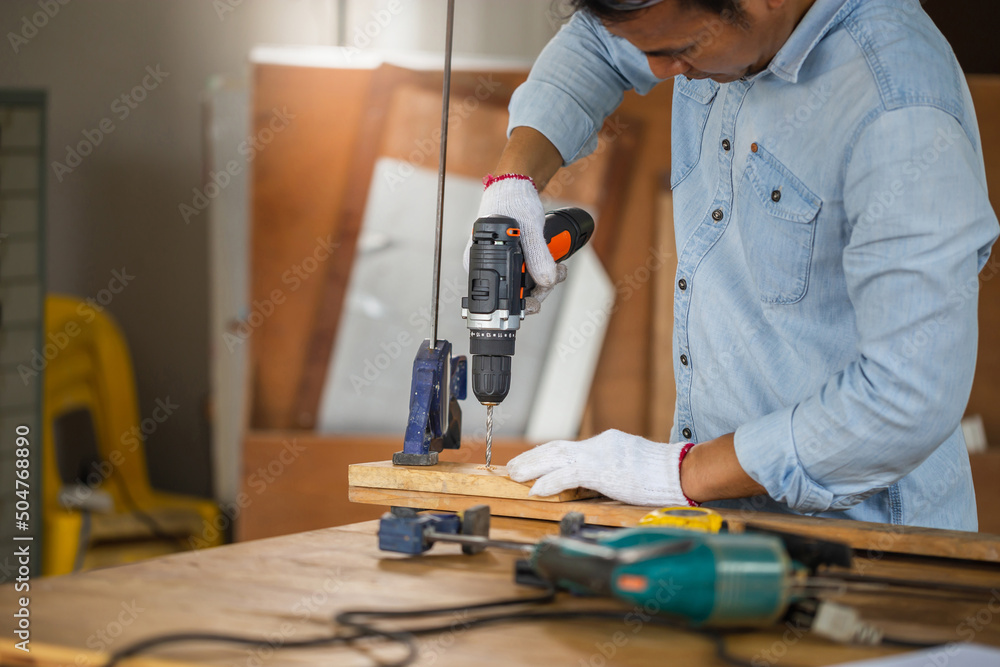 Carpenter drilling a hole in timber, Carpenter working on woodworking machines in carpentry shop, male carpenter drilling a hole in wooden plank on workbench. Carpenter drilling a hole in timber, Carpenter working on woodworking machines in carpentry shop, male carpenter drilling a hole in wooden plank on workbench.