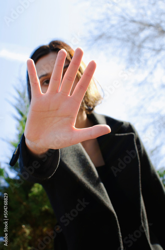 portrait of young woman extending hand forward saying no enough against the sky. female palm close up raised in prohibiting gesture. shows stop sign prohibition symbol keeps palm forward to camera.