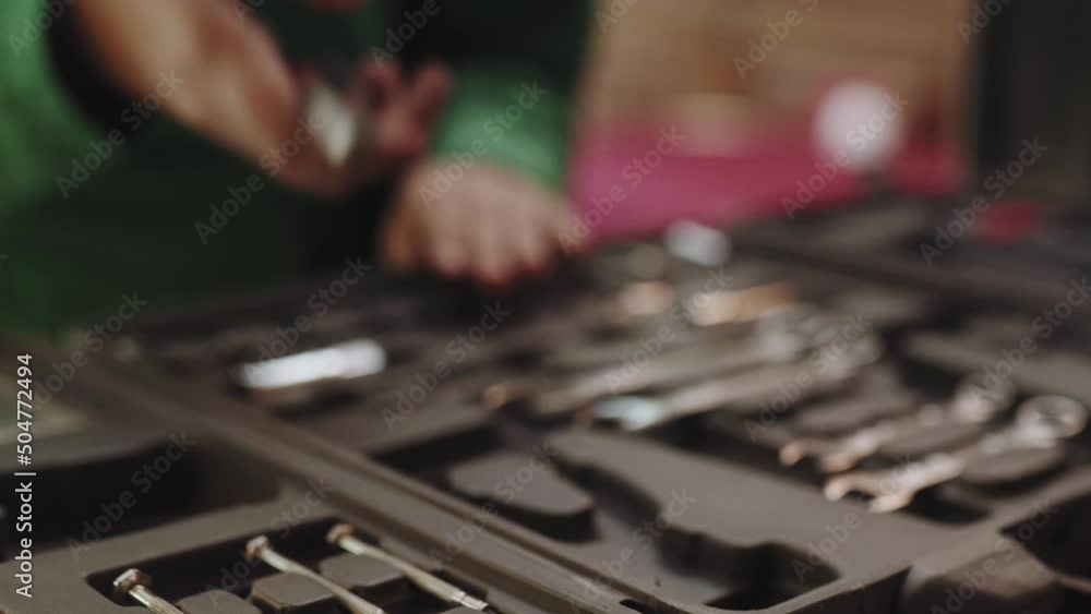 Master puts a wrench into a tool box and takes pliers from it. Woman mechanic takes instruments for car repair job. Master puts a wrench into a tool box and takes pliers from it. Woman mechanic takes instruments for car repair job.