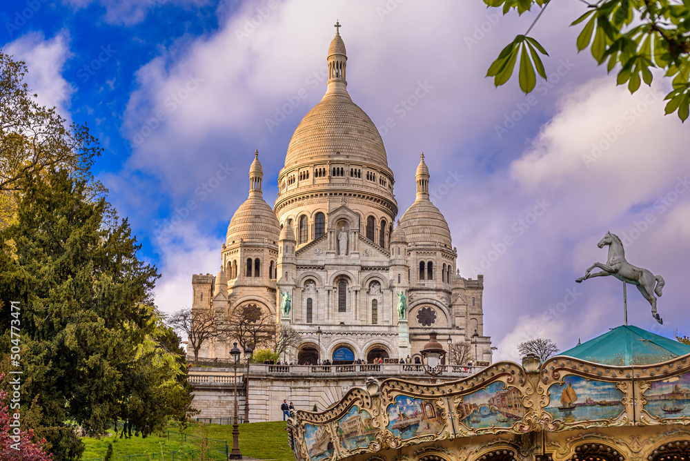 Purple cloudy twilight above the Sacré-Coeur Basilica on the top of the Montmartre hill with a carousel in the bottom right corner