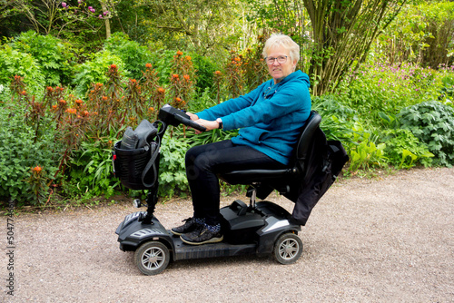 Canvas-taulu Blond haired woman on mobility scooter smiles happily as she enjoys the freedom being outdoors on a spring day that the scooter allows her despite her disability