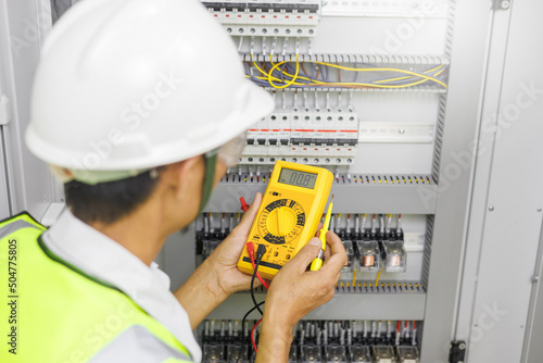 Electrical engineer or repairman holding digital multimeter and looking at the screen to inspecting the electrical system in a factory.