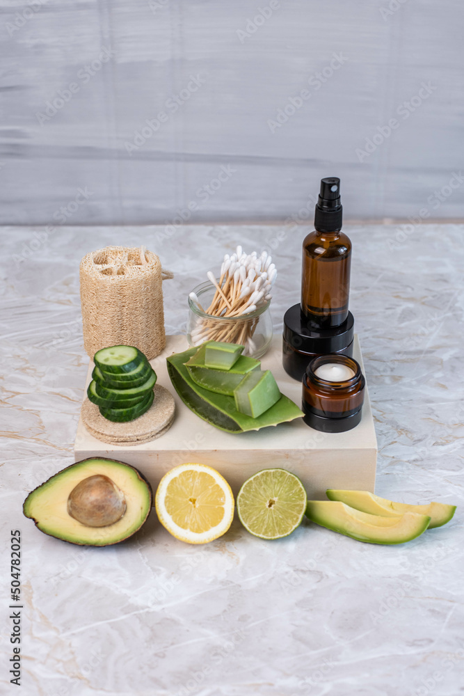 Naklejka premium Braunglasflasche und Tiegel mit Creme, hausgemachte Gesichtspflege, natürlich, mit Gurke, Avocado, Aloe Vera, Limette und Zitrone, feuchtigkeitsspendende Gesichtspflege, Q-Tips aus Bambus