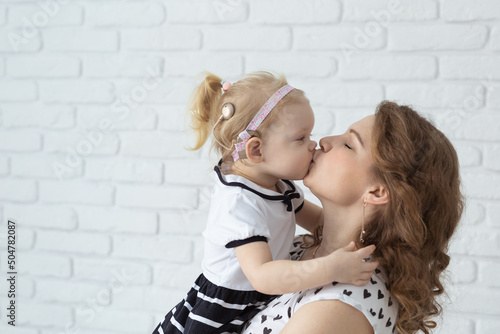 Mother holds and having fun her child with hearing aids and cochlear implants on white brick wall with copy space and place for advertising . Deaf and innovating medicine technologies concept photo