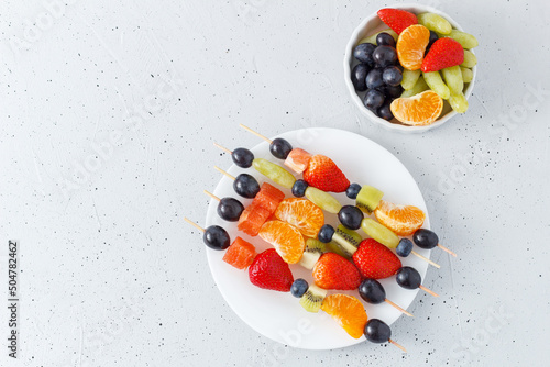 Fresh fruit skewers on a plate for a healthy snack on a gray background. copy space