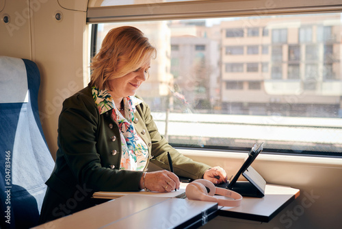 Woman works from a train with a tablet and a notebook. Working remotely, travel