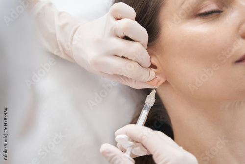 Doctor cosmetologist making beauty injection in woman ear photo