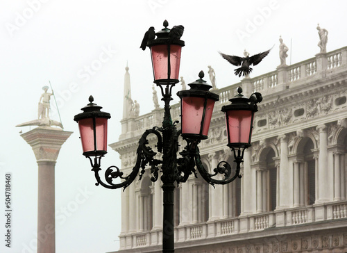 Romantic view of a typical Venetian lamppost with doves. In the background, the Marciana Library and the column of San Teodoro wrapped in mist photo