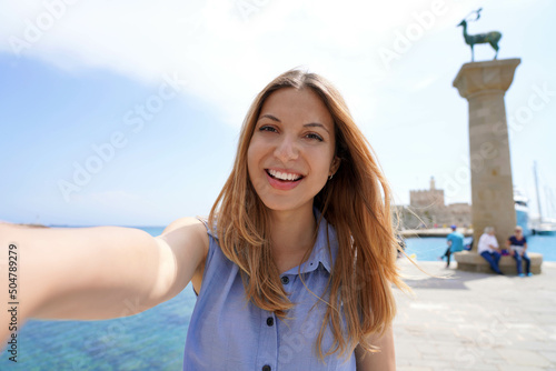 Close-up of happy girl taking self portrait with deer statue landmark of Rhodes city in Greece
