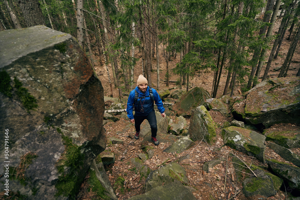 Caucasian male backpacker moving up path among rocks Caucasian male backpacker moving up path among rocks
