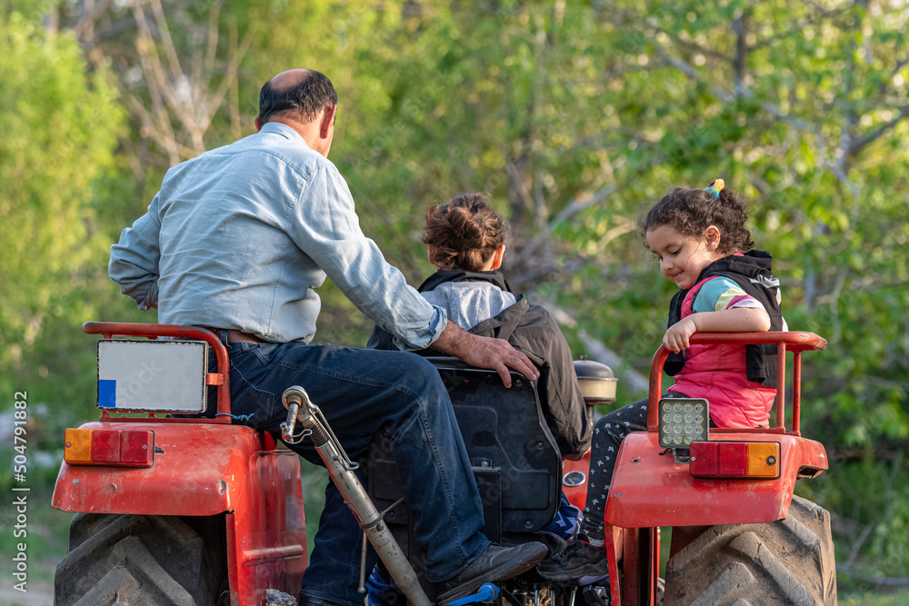 Fototapeta premium Selective focus shot of mother, grandfather and little girl walking with tractor.