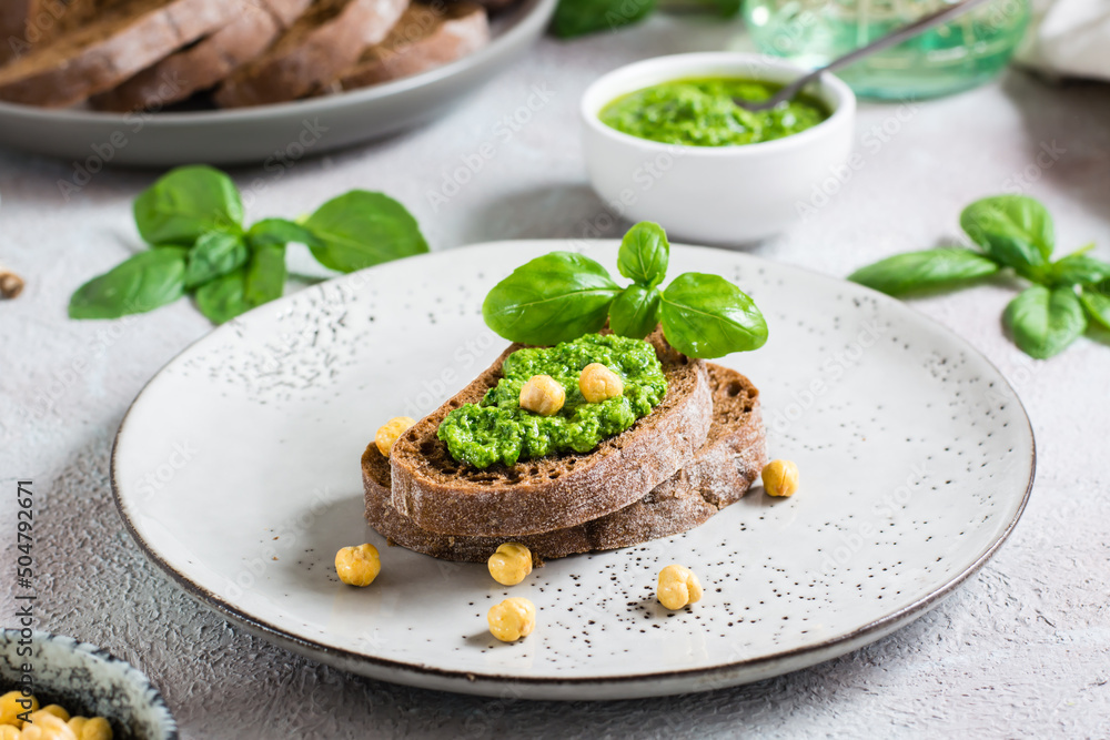 Fresh sandwich with pesto and chickpeas on rye bread on a plate on the table. Fresh sandwich with pesto and chickpeas on rye bread on a plate on the table.