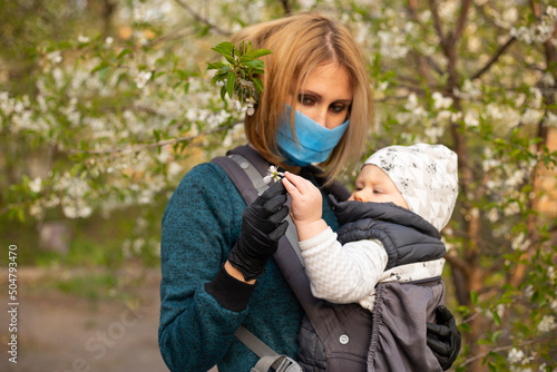 young mother in mask and little baby boy son having fun in spring park near blooming tree. Spring concept