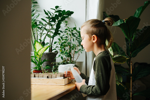 Side view of a boy standing next to a window sill, holding a spray bottle photo