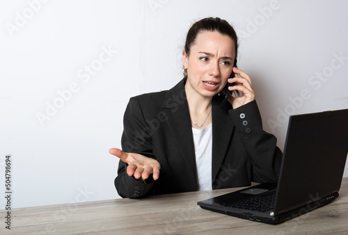 ragazza arrabbiata  che lavora al computer  mentre telefona col cellulare photo