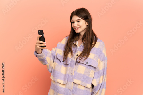 Young Ukrainian girl isolated on pink background making a selfie