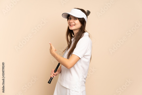 Young Ukrainian golfer girl isolated on beige background pointing back