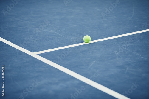 Minimal background image of single yellow tennis ball on blue flooring at tennis court, copy space © Seventyfour
