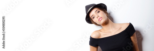 Portrait of beautiful fashionable girl in black clothes and wearing hat posing against white wall © Solid photos