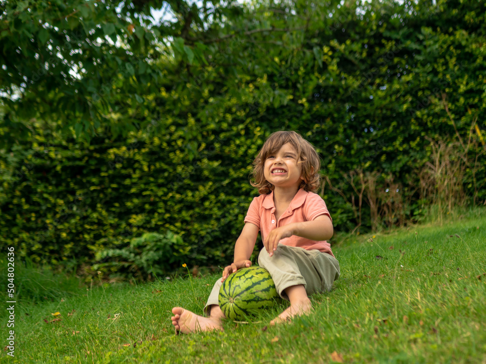 A little toddler boy is eating fresh watermelon on a sunny day on his summer holidays at the countryside in a cottage in England