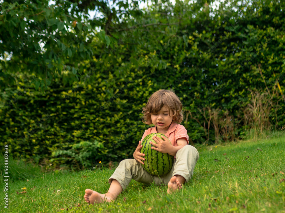 A little toddler boy is eating fresh watermelon on a sunny day on his summer holidays at the countryside in a cottage in England A little toddler boy is eating fresh watermelon on a sunny day on his summer holidays at the countryside in a cottage in England