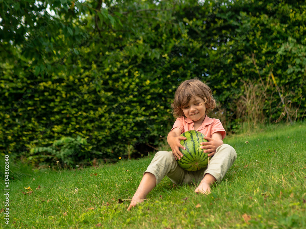 A little toddler boy is eating fresh watermelon on a sunny day on his summer holidays at the countryside in a cottage in England A little toddler boy is eating fresh watermelon on a sunny day on his summer holidays at the countryside in a cottage in England