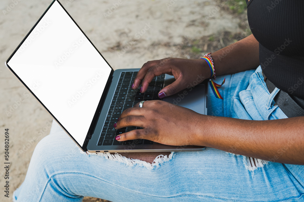 Naklejka premium Close-up of African American woman's hands using laptop computer, sitting on park bench. Mockup.
