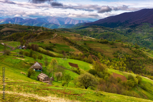 green carpathian landscape in spring time. beautiful mountain landscape with rural valley and village in the distance. clouds on the sky above the borzhava ridge