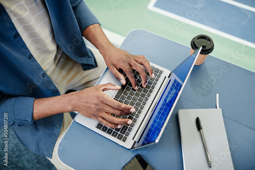Fototapeta Naklejka Na Ścianę i Meble -  Top view closeup of black man using laptop and typing while working in sports training center