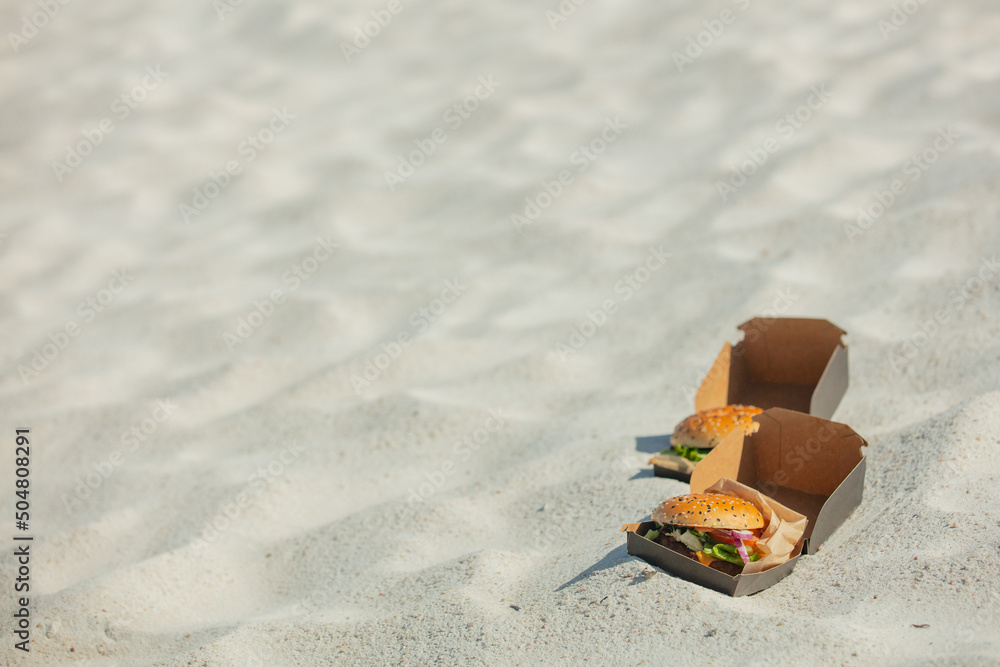 Naklejka premium Tasty burger in box on white sand on beach