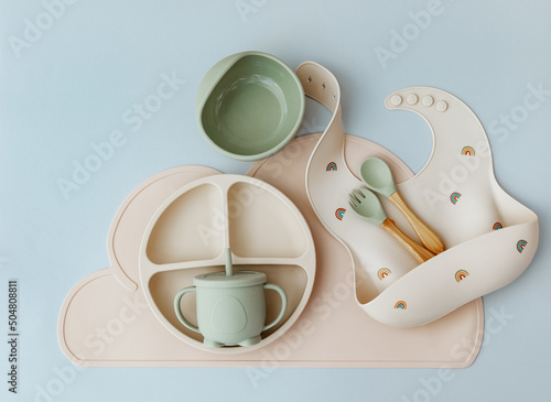 Set of silicone dishware and baby accessories on blue light background, flat lay photo