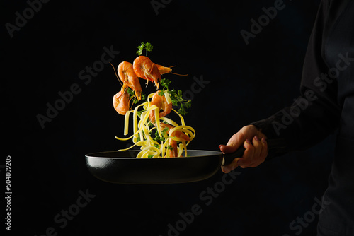 Shrimps with pasta and vegetables in a pan in a frozen flight on a black background. Sea food. Healthy vegetarian food. Organic gourmet food. Banner, advertisement, invitation.