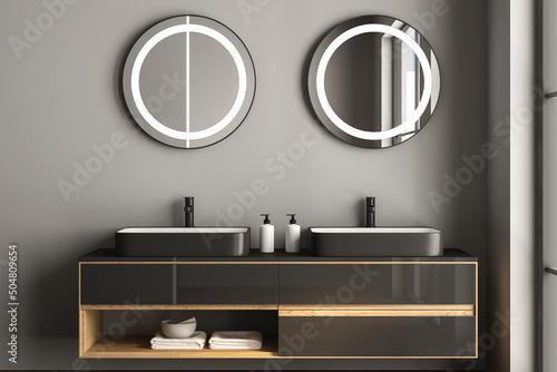 Close up of double sink with oval mirrors hanging in on dark gray wall, modern cabinet with black faucets in minimalist bathroom. 3d rendering