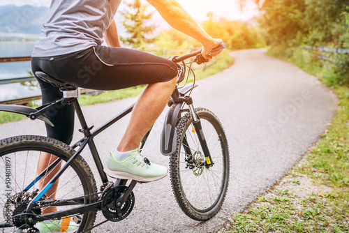 Close-up photo of a man dressed in cycling clothes starting riding a modern bicycle on the asphalt out-of-town bicycle path. Active sporty people concept image.