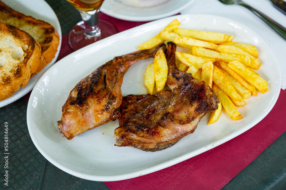 Appetizing grilled rabbit pieces with vegetable garnish of fried potatoes .