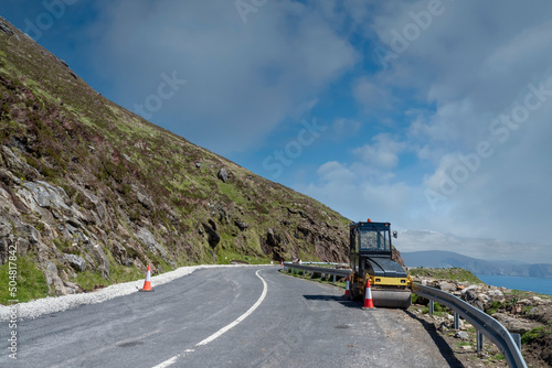 Road works in a mountain area. Small drum asphalt compactor. Warm sunny day. Achill island, county Mayo, Ireland. Transportation industry. High way repair.