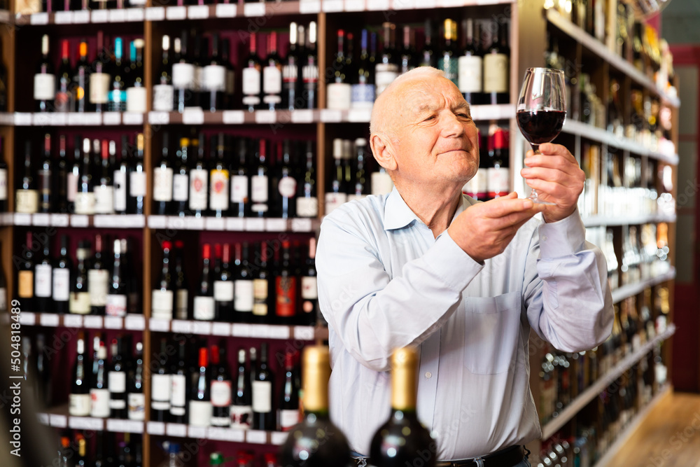 Elderly man checks the color and taste of red wine in a liquor store. High quality photo