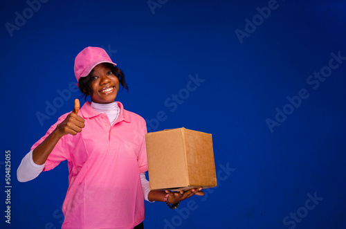 Tablou canvas beautiful african female courier worker holding a box, does a thumbs up gesture