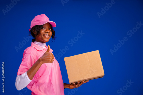 Tablou canvas beautiful african female courier worker holding a box, does a thumbs up gesture