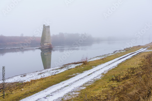 Concrete support of the blown up bridge on the river in damp foggy weather. Consequences of the war. Background photo