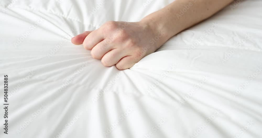 Woman hand tightly squeezes sheet on bed Woman hand tightly squeezes sheet on bed