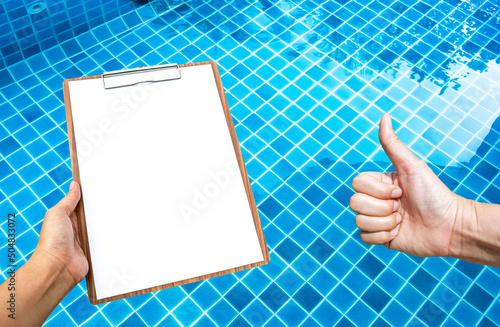 Blank paper on wooden clipboard with girl hand over crystal clear swimming pool water, water quality check, swimming pool maintenance and service concept
