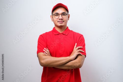 Close-up of confident smiling asian male courier in red uniform and cap, smiling determined, cross arms chest
