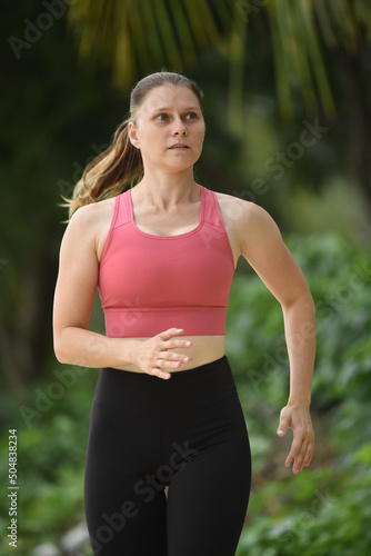 Portrait of a 30-year-old woman jogging outdoors. A girl runs along the beach in a pink bra. The concept is a healthy lifestyle, weight loss, hobbies, sports training, outdoor activity. Front view © Nina