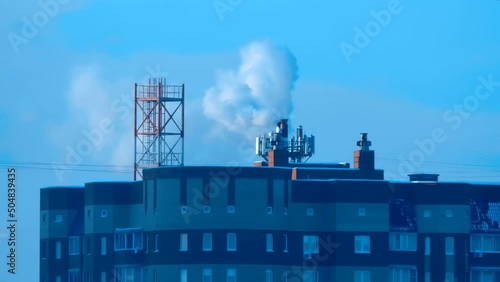 Puffs of steam from a pipe of a gas boiler house that heats a microdistrict of brick high-rise buildings in a cold winter photo